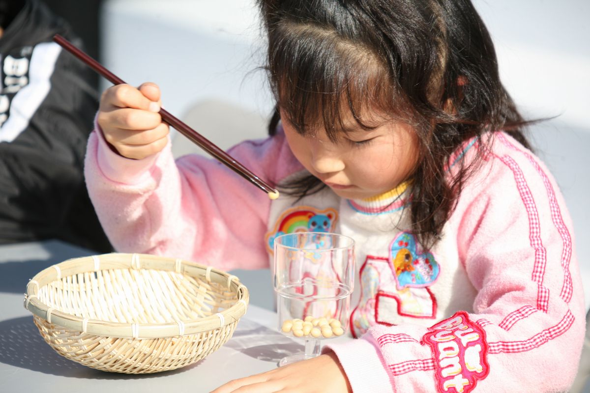 豆つかみゲーム大会に参加し、箸でつかんだ豆を真剣な顔でコップに移す女の子