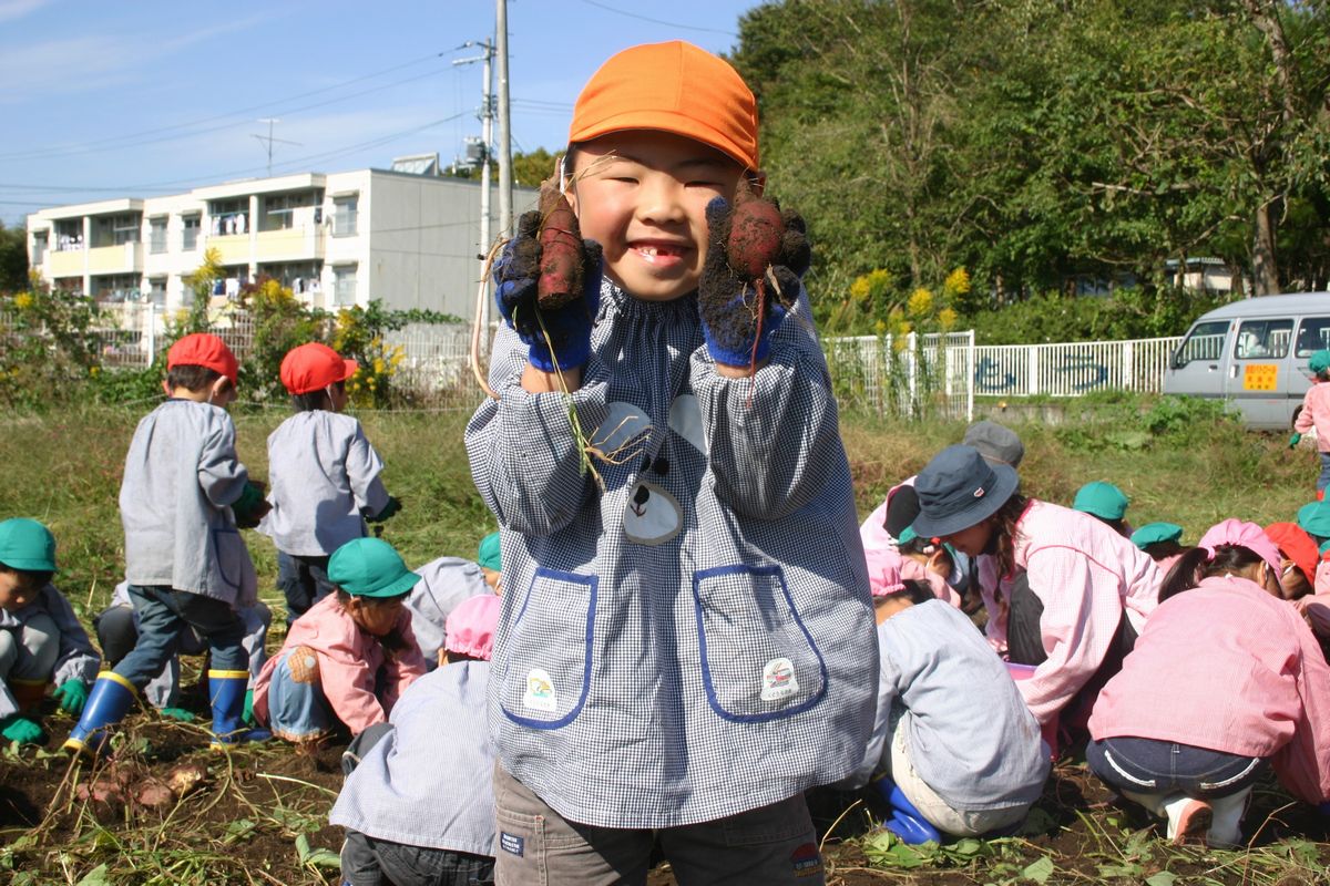 両手に自分で掘ったサツマイモを持ち満面の笑顔を見せる園児