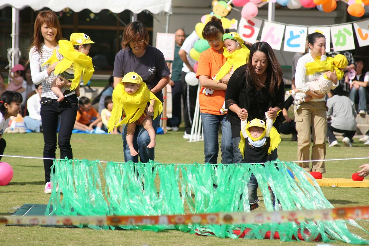 ひよこの衣装と帽子をかぶり、お父さんお母さんに抱っこされてゴールする園児