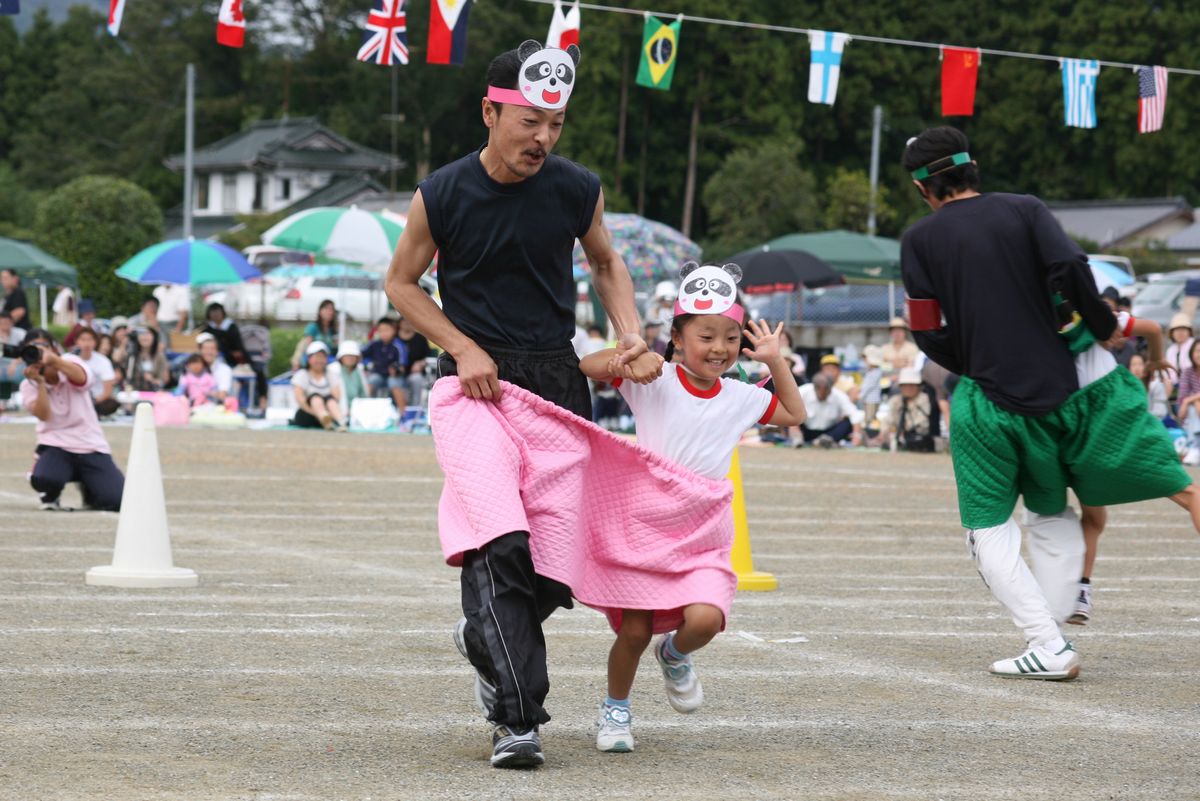 お父さんと手をつなぎ、1つのスカートを二人で履いて笑顔で走る園児たち