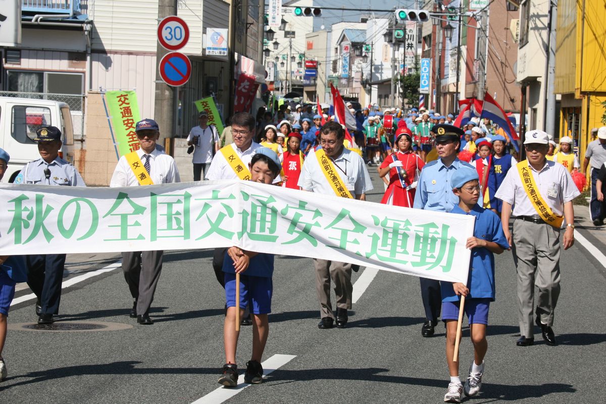 「秋の全国交通安全運動」と書かれた横断幕を先頭に、駅前通りをパレードする熊町小学校鼓笛隊