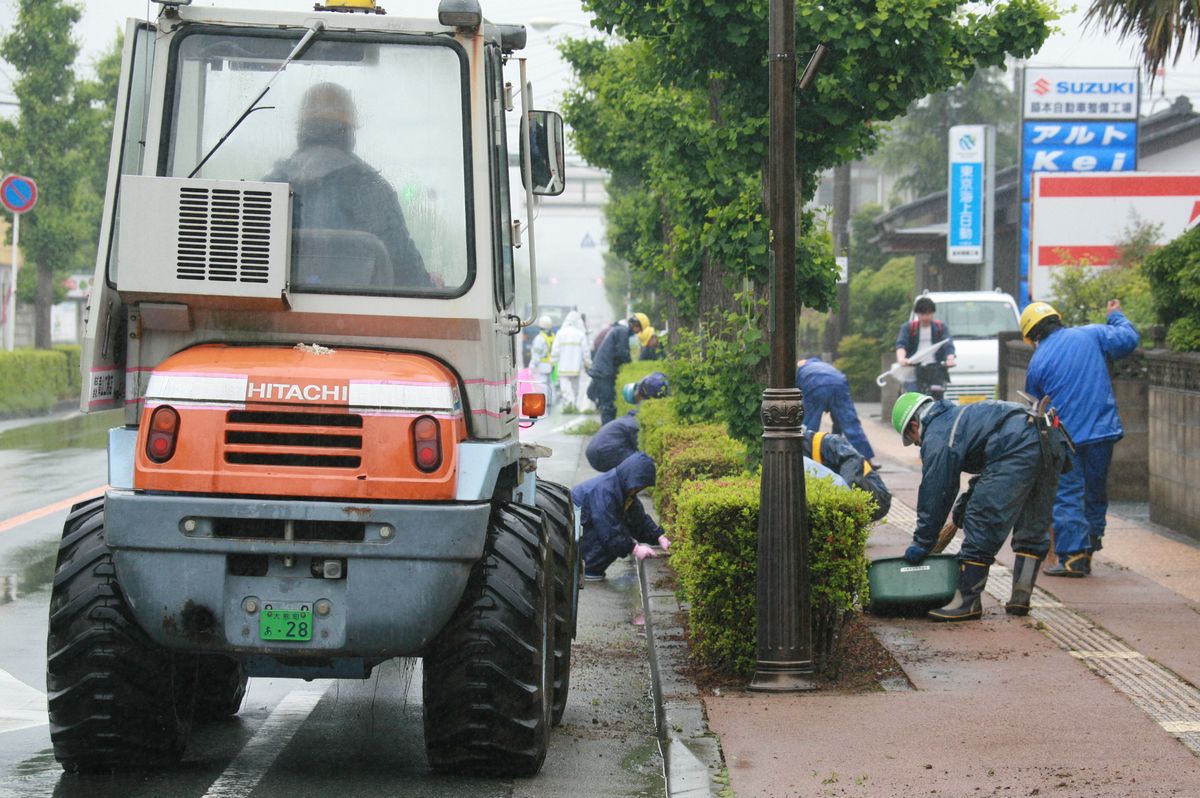小雨の降る中、歩道の除草作業や投げ捨てられた空き缶や空き瓶などのゴミ拾いをする参加者