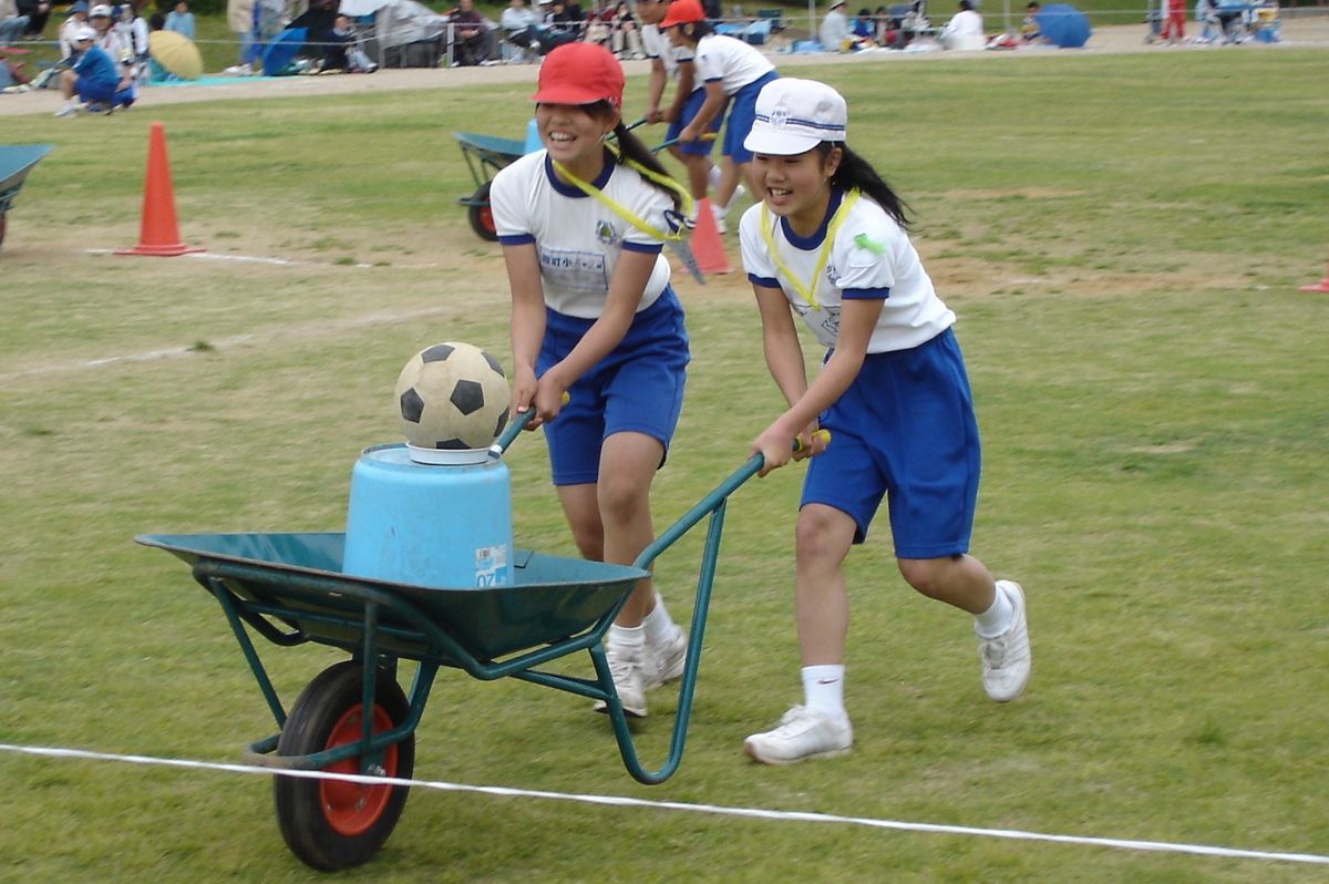 リヤカーの荷台にサッカーボールを乗せて落ちないように慎重に走る2人組
