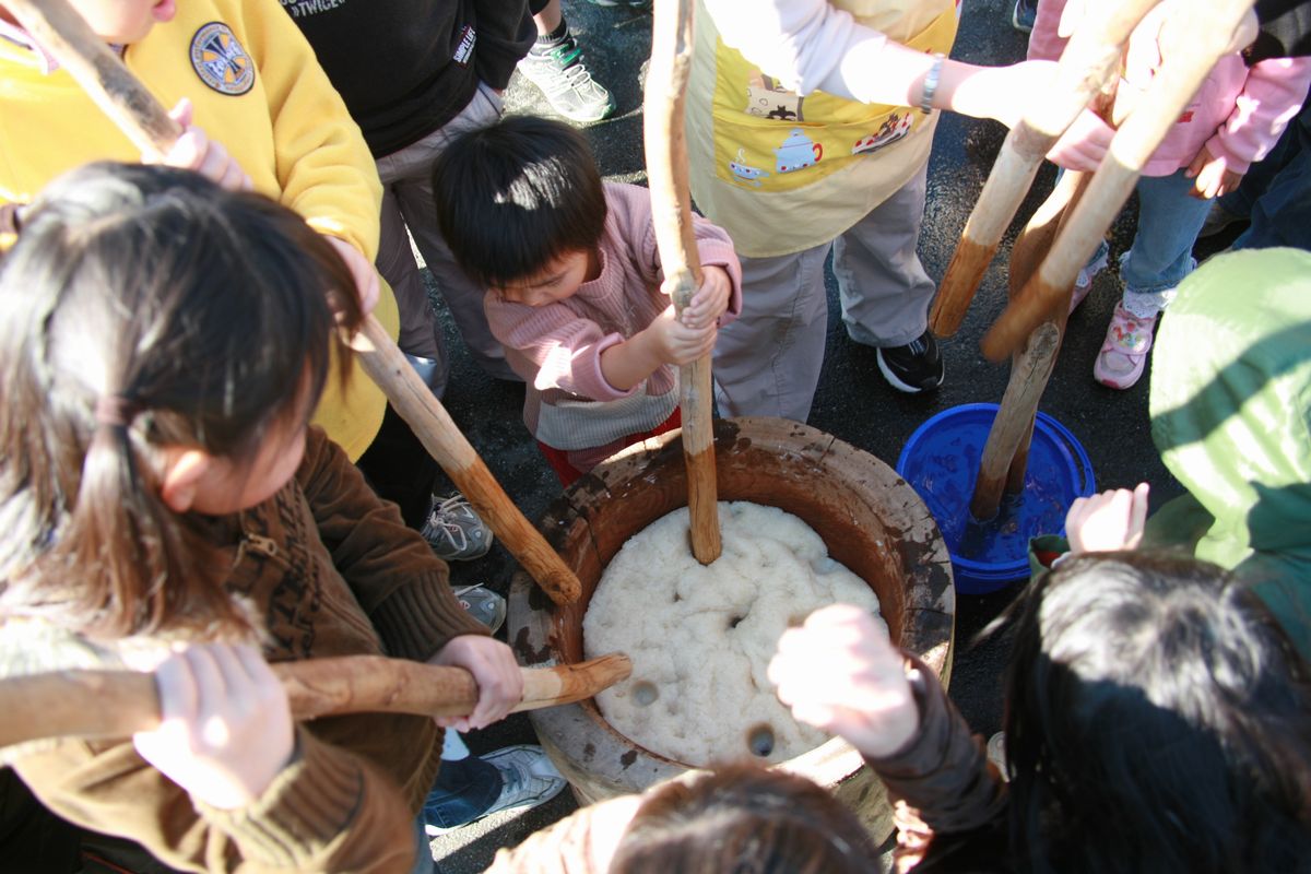 大きな臼と杵でもちつきをする子どもたち