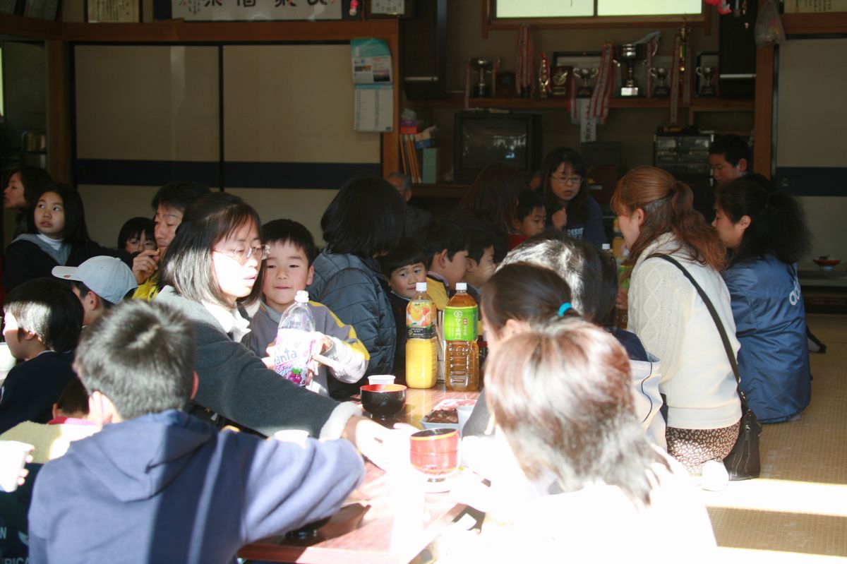 大きな稲穂が飾られた熊川地区集会場の大広間でつきたての餅を食べる参加者たち