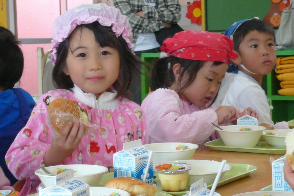 給食のハンバーガーを持ってかわいらしく微笑む園児