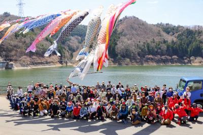 おおくまコミュニティづくり実行委員会は4月9日、町内大川原地区で春の坂下ダムウォーキングイベントを開催。イベント参加を記念して、坂下ダムを背景に鯉のぼりの下で記念撮影を行いました。